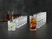 Ein 12-teiliges Becherset im Ethno-Stil, bestehend aus klaren, strukturierten Gläsern, die auf einer dunklen Oberfläche in einer diagonalen Anordnung präsentiert werden. Im Vordergrund sind zwei Gläser mit Getränken und Eiswürfeln zu sehen.