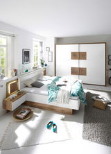 Moderne Schlafzimmeransicht mit einem weißen Bett und einem Schwebetürenschrank in Holz- und Weißtönen, von der Seite betrachtet.