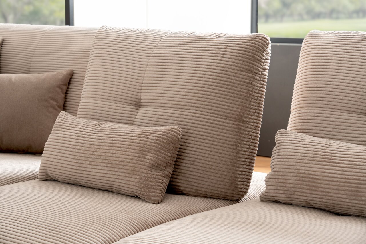 Close-up van een beige hoekbank met geribbelde bekleding en meerdere kussens, gezien vanaf de zijkant.