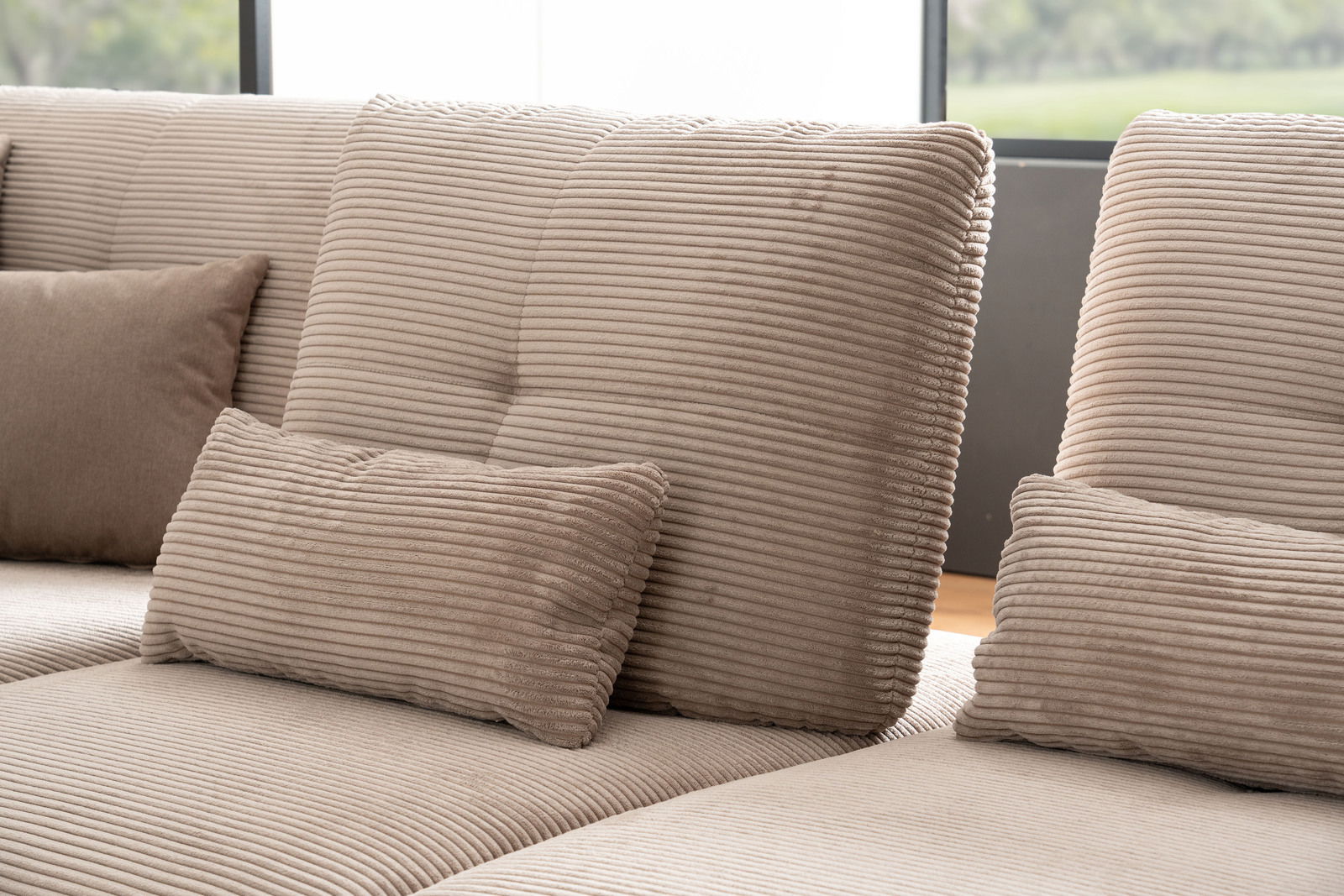 Nahaufnahme einer beigen Rundecke mit geripptem Stoff und mehreren Kissen, seitliche Perspektive.