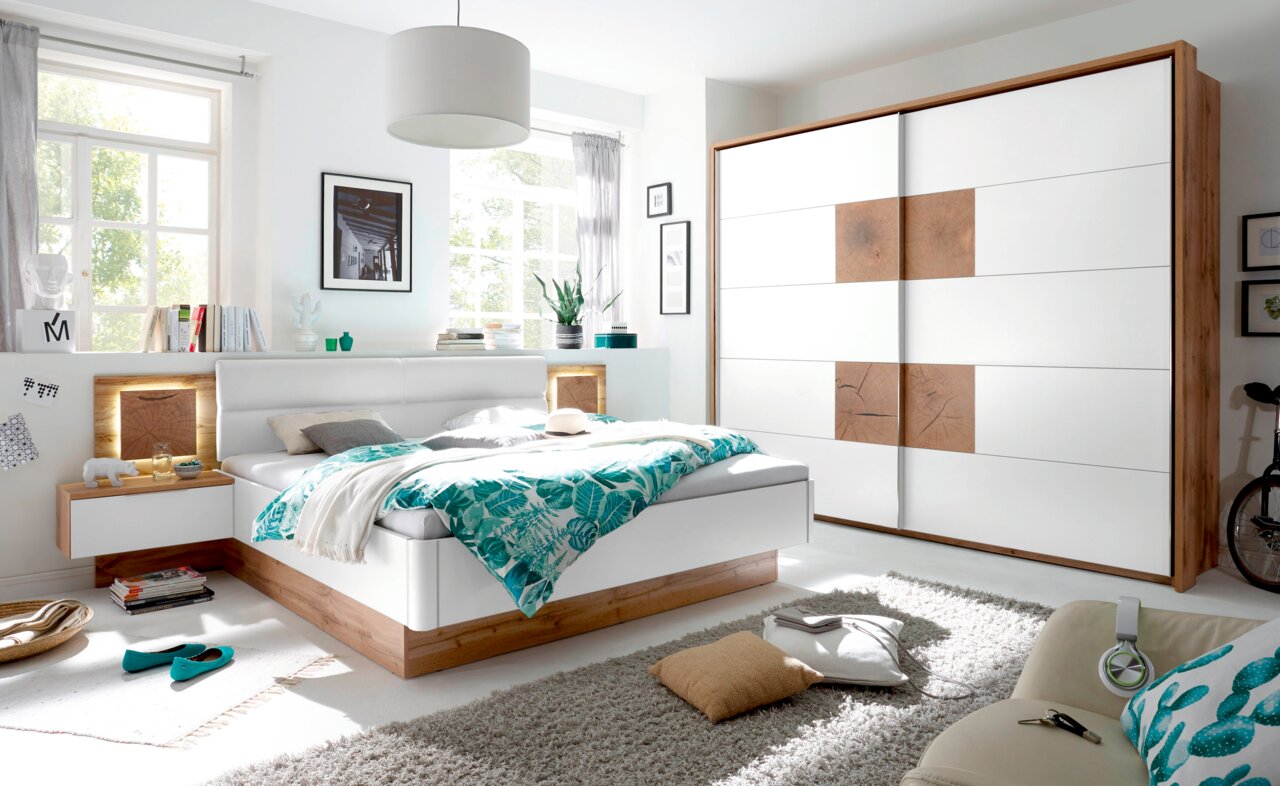 Modernes Schlafzimmer mit einem Schwebetürenschrank in Holz- und Weißoptik, seitliche Perspektive.