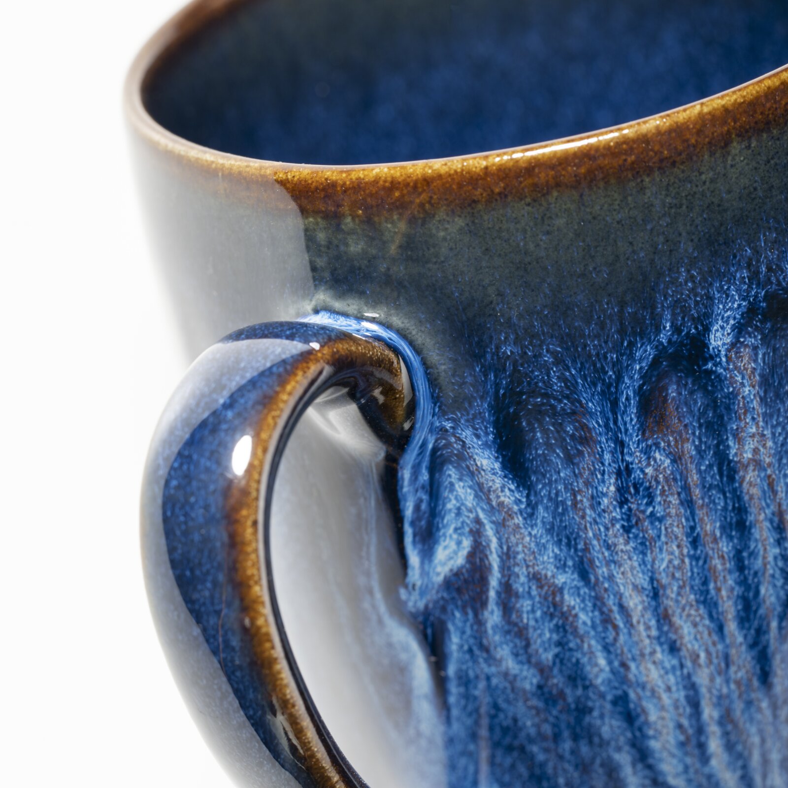 Makro-Nahaufnahme einer glasierten Keramik-Tasse in Blau mit braunem Rand und sichtbarem Henkel, perspektivisch schräg von oben auf den oberen Rand und die Außenseite fotografiert.