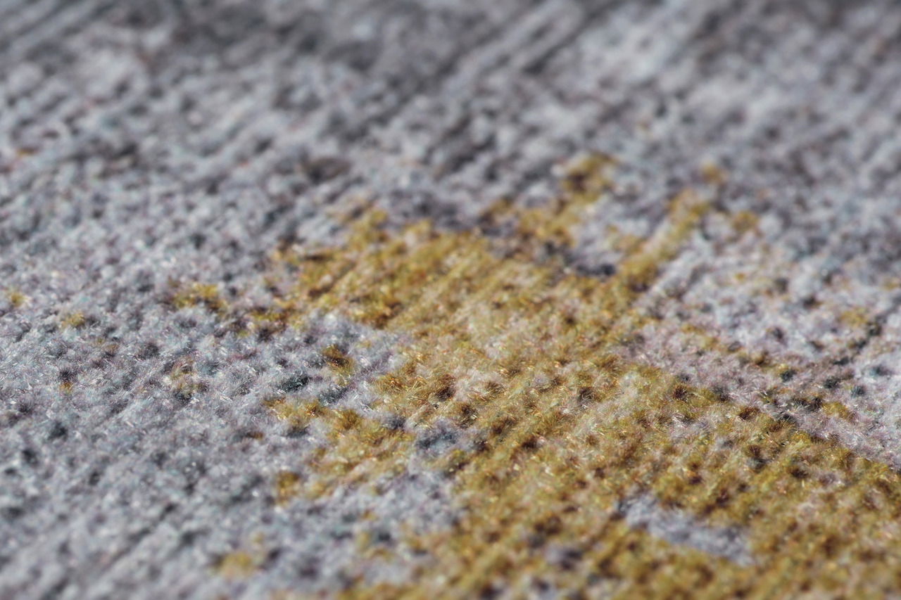 Nahaufnahme eines Teppichs mit gemustertem Design in Grau- und Gelbtönen, perspektivisch von der Seite aufgenommen.