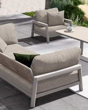 Een moderne loungebank en fauteuil op een terras, gezien vanaf de zijkant, met comfortabele kussens en een tafeltje met een koffiekopje.