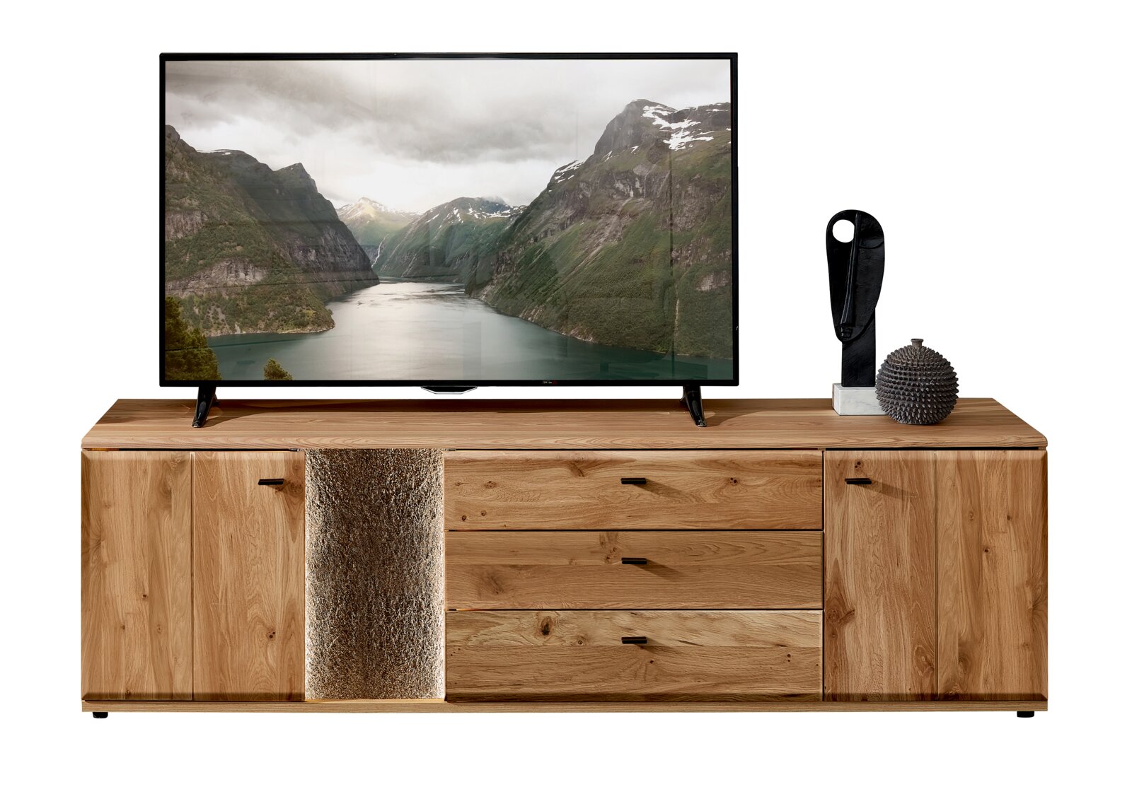Cantus Lowboard REIMS Frontansicht eines breiten TV-Lowboards aus hellem Massivholz mit zwei seitlichen Türen und drei Schubladen, mittigem Akzent in Steinoptik und schwarzen Griffen, darauf ein Fernseher und Dekoration