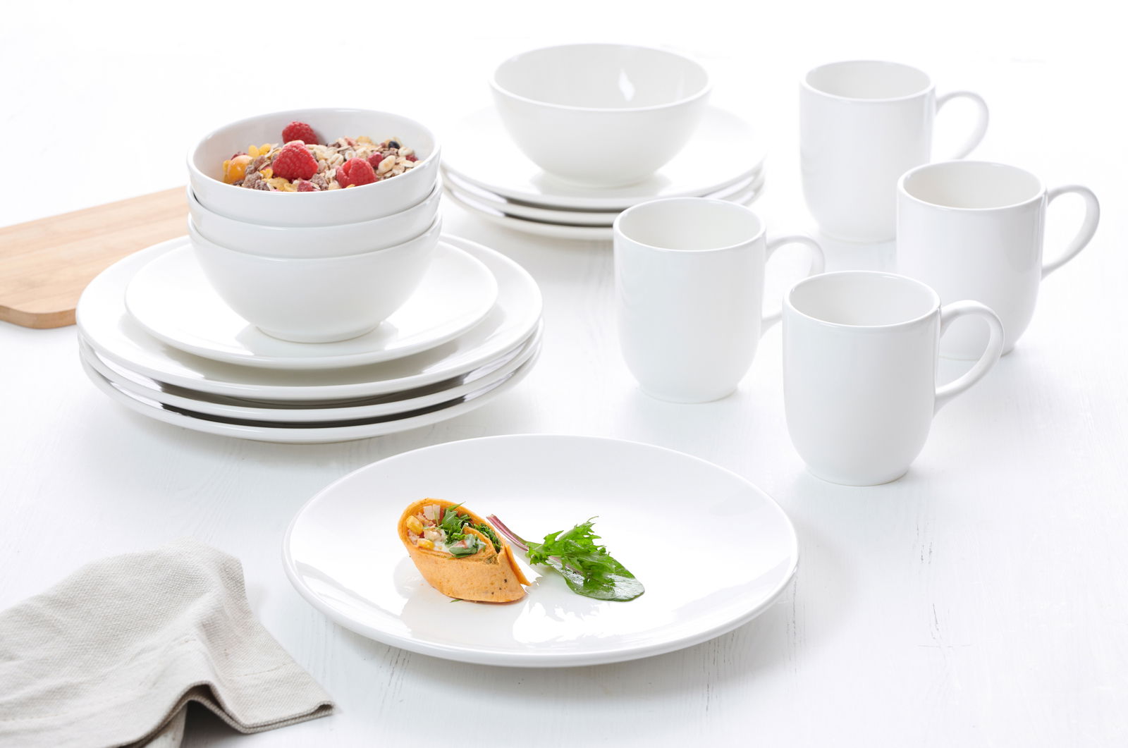 Weißes 16-teiliges Kombiservice Lund, bestehend aus Tellern, Schalen und Tassen, auf einem Tisch arrangiert, seitliche Perspektive.