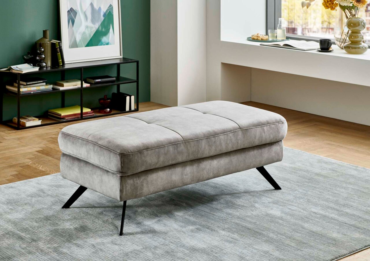 Beldomo System XXL-Hocker MAGGIA Grauer XXL-Hocker mit schwarzen Metallbeinen in einem modernen Wohnzimmer, seitliche Perspektive.