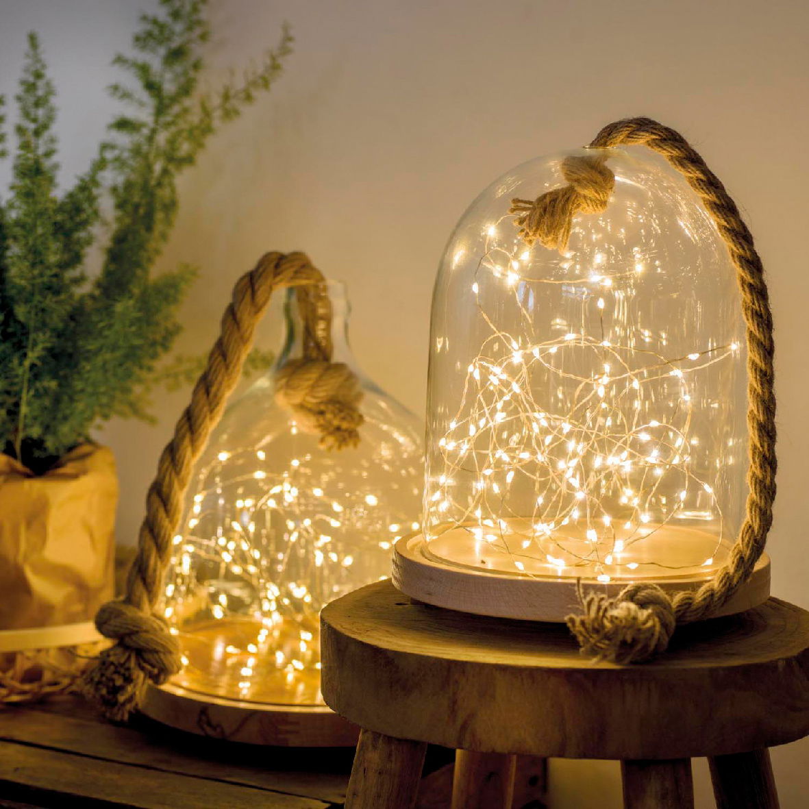 LED-Lichterkette in einer Glasglocke mit Seil, auf einem Holzhocker stehend, seitliche Perspektive