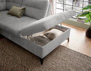 Graues Ecksofa mit Stauraum, geöffnet, von schräg oben fotografiert. Ein Kissen liegt auf der Sitzfläche, und im Stauraum sind weitere Kissen sichtbar.