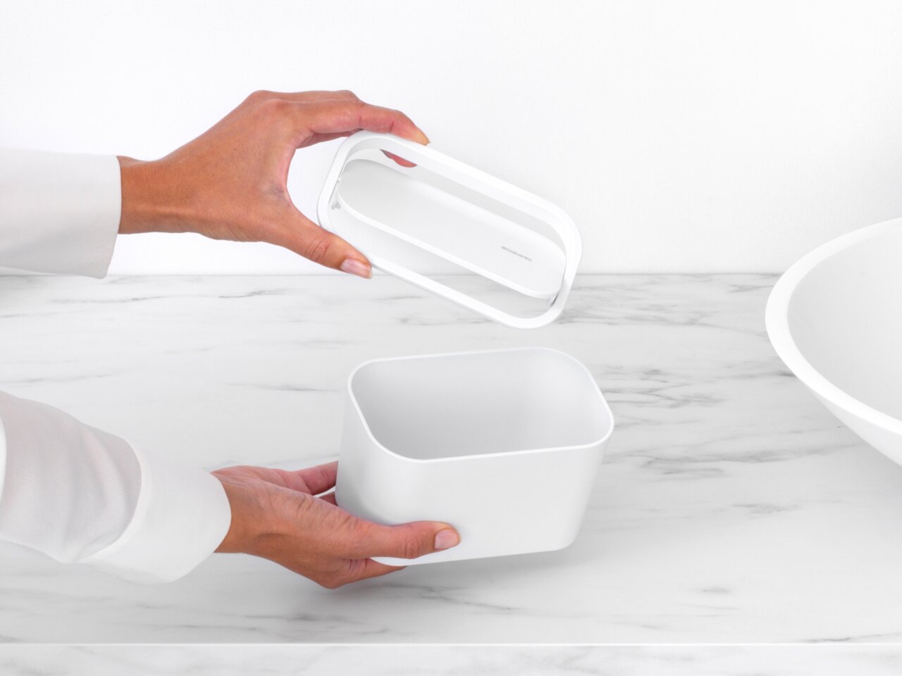 Weiße Abfallbehälter mit abnehmbarem Deckel, auf einer Marmoroberfläche, aus der Vogelperspektive betrachtet.