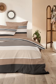 Gestreepte beddengoed in beige, grijs, wit en zwart met twee kussens op een bed in de slaapkamer, gefotografeerd vanuit een schuin vooraanzicht.