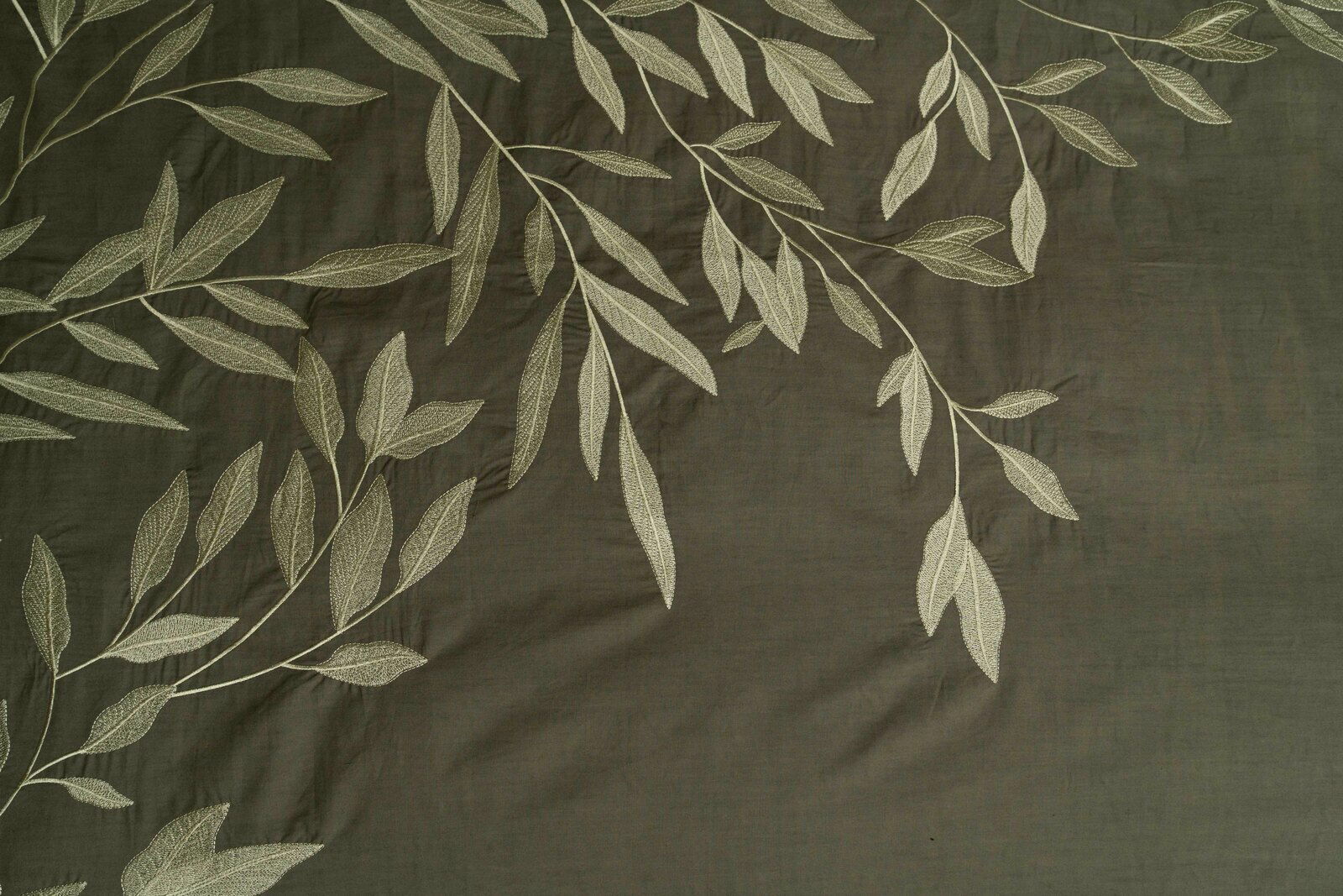 Bettwäsche mit elegantem Blattmuster in Nahaufnahme, dunkelgrüner Hintergrund mit hellen Blättern.