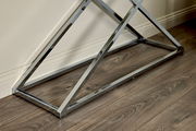 Nahaufnahme eines modernen, verchromten Tischgestells auf einem Holzboden, seitliche Perspektive.