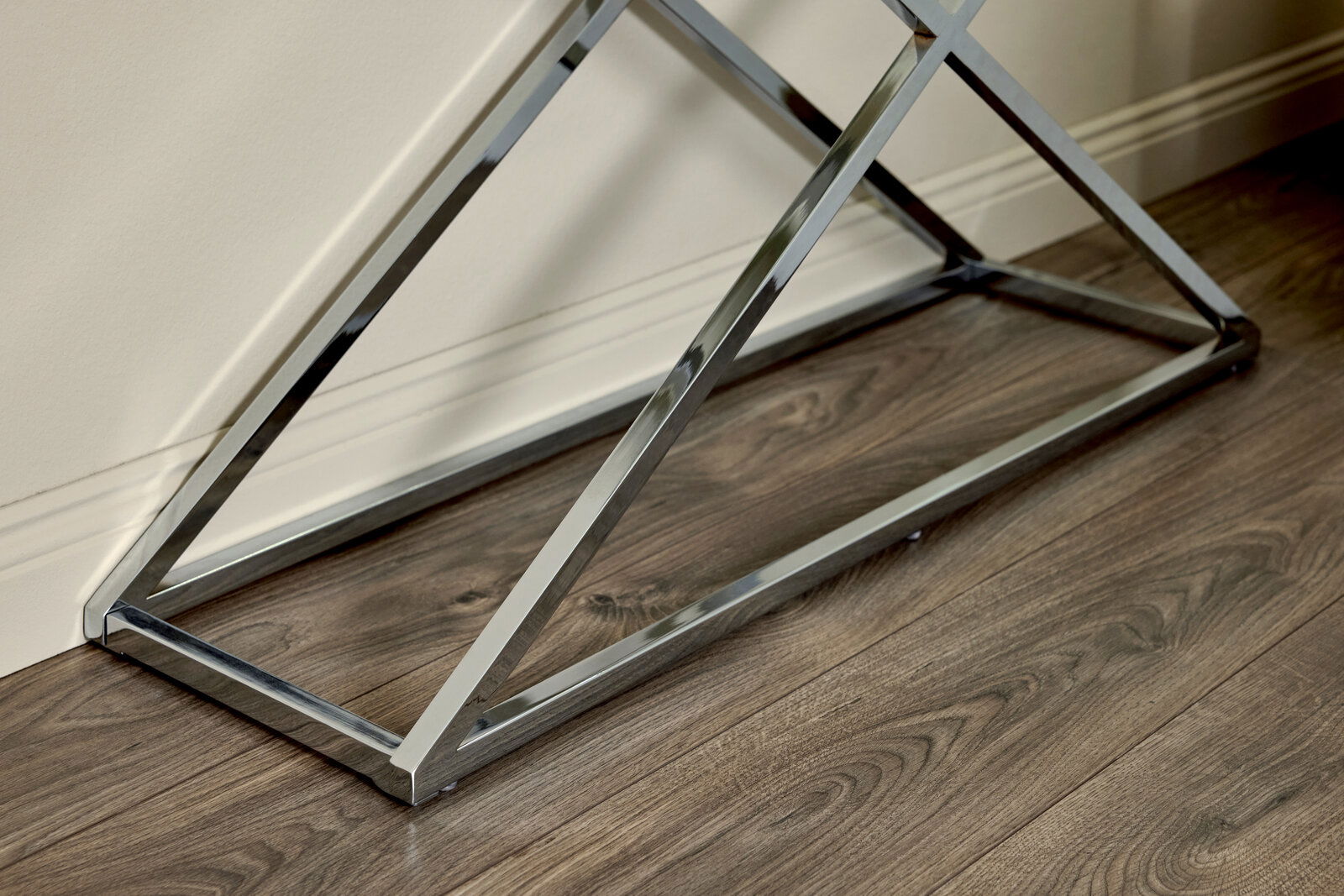Nahaufnahme eines modernen, verchromten Tischgestells auf einem Holzboden, seitliche Perspektive.