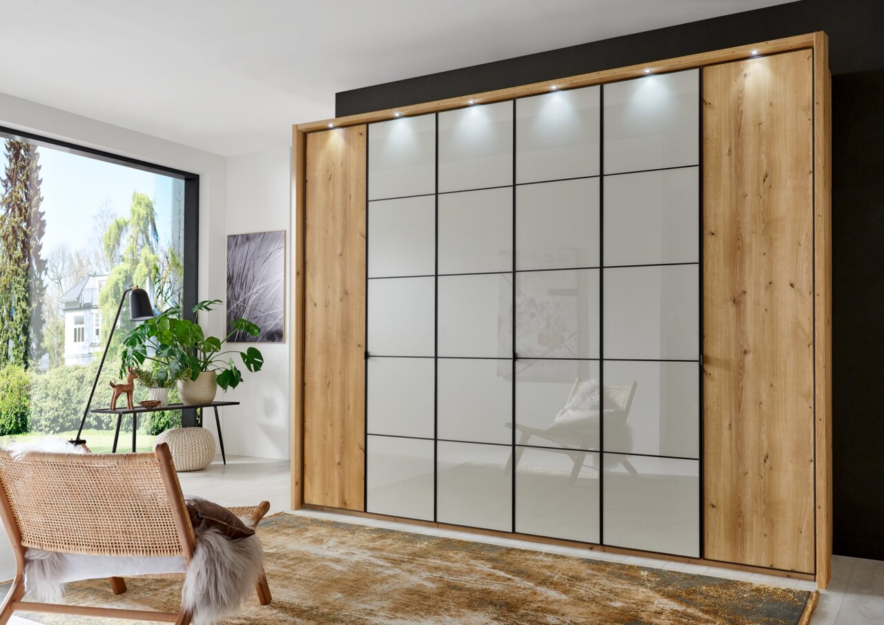 Novel Passe-partoutlijst QUITO Moderne draaideurkast met houten frame en glazen deuren, van bovenaf verlicht, in een stijlvol ingerichte ruimte, gezien vanaf de voorkant van de kast.