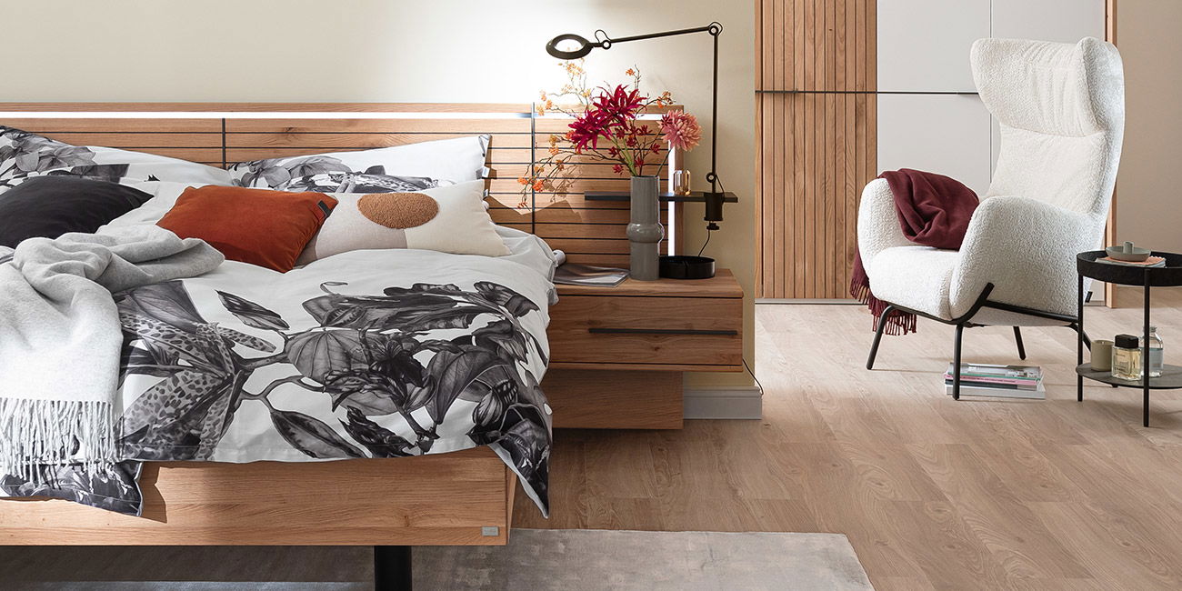 Schlafzimmer mit Holzbett, schwarz-weißer Bettwäsche, Sessel und Deko.