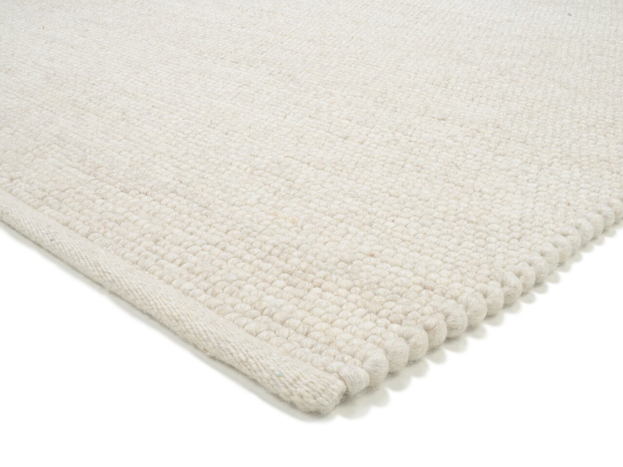 Nahaufnahme eines weißen, handgewebten Teppichs mit strukturierter Oberfläche, von der Seite fotografiert.