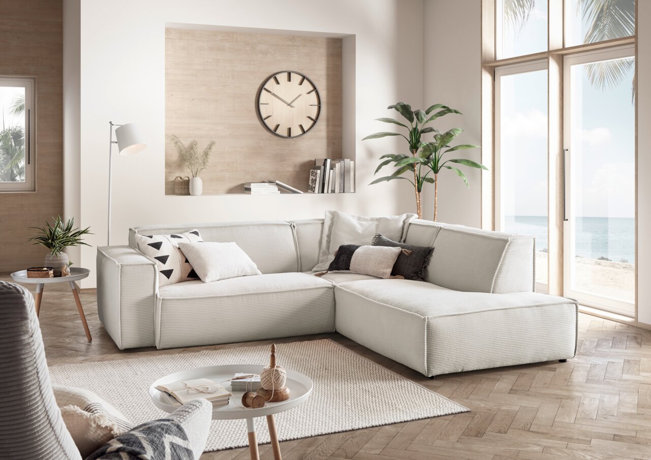 Eckkombination Sofa in einem modernen Wohnzimmer mit Blick auf das Meer durch große Fenster, helle und gemütliche Atmosphäre