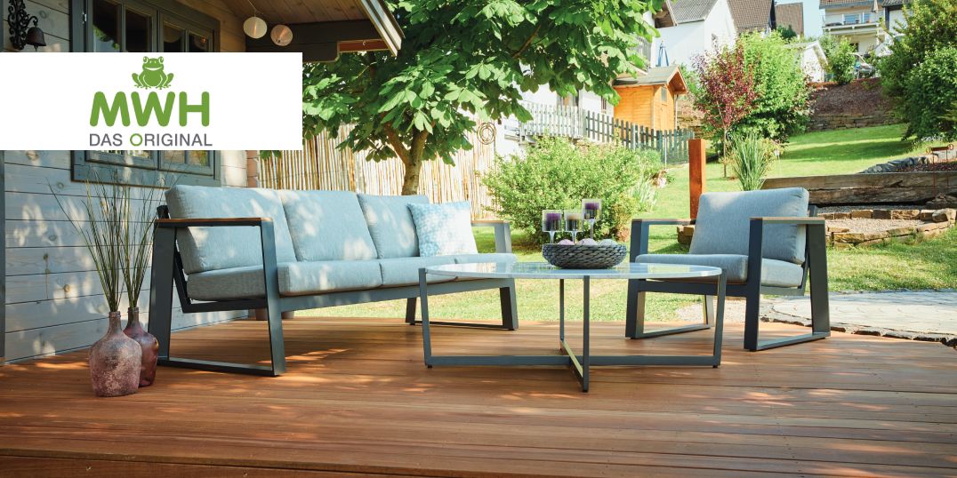 Ein Sitzbereich im Garten mit einem grauen Sofa und einem Sessel auf einer Holzterrasse. Logo MWH Das Original