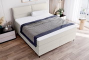 Boxspringbett in einem modernen Schlafzimmer, seitliche Perspektive, mit hellem Kopfteil und stilvoller Bettwäsche.