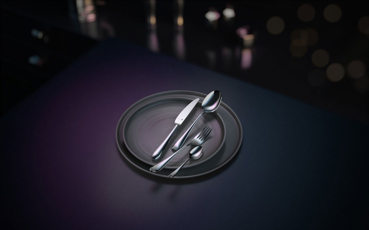 Elegantes Besteckset auf einem dunklen Teller, bestehend aus Messer, Gabel, Löffel und Teelöffel, aus der Vogelperspektive fotografiert.