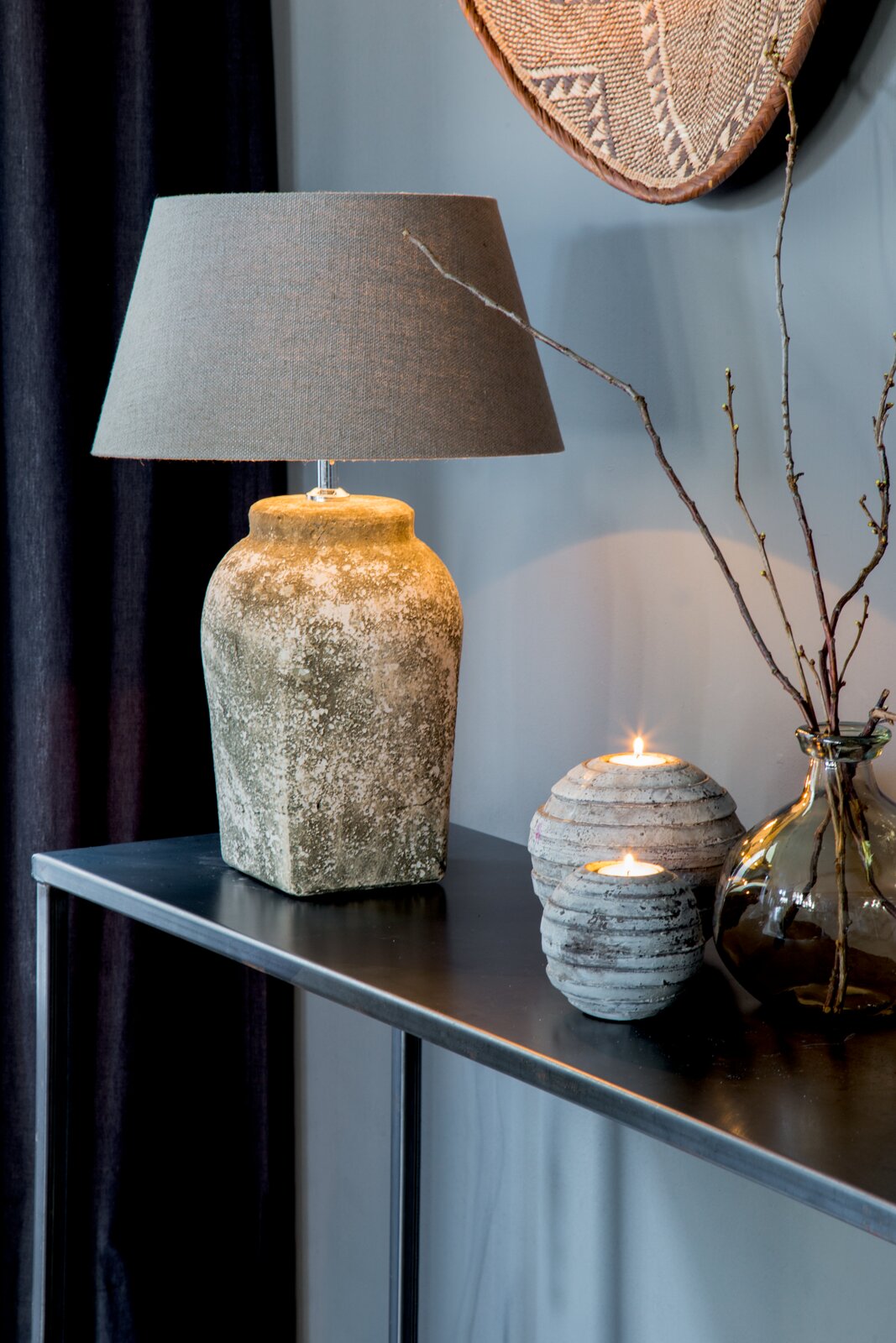 Rustieke tafel met een staande lamp met een ronde, grijze lampenkap en een gestructureerde keramische voet, gezien vanaf de zijkant.