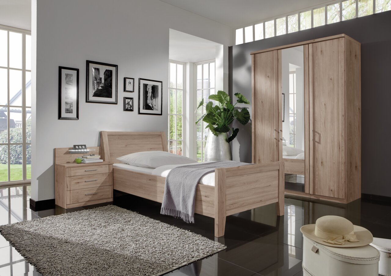 Komfortbett aus hellem Holz in einem modernen Schlafzimmer, seitliche Perspektive mit Nachttisch und Kleiderschrank.