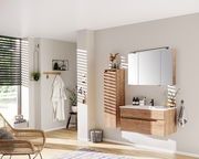 Moderner Badezimmer-Mittelschrank aus Holz, links neben einem Waschbeckenunterschrank und einem Spiegelschrank, aus seitlicher Perspektive fotografiert.