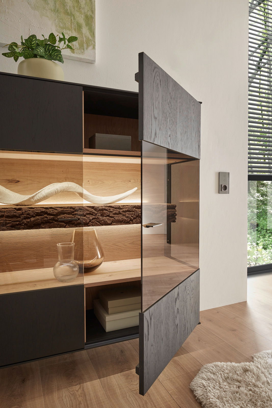 Geöffnetes Highboard mit dunkler Holzfront, dekorativen Elementen und Pflanzen, seitliche Perspektive