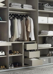 Offener Kleiderschrank mit hängender Kleidung, Regalen mit gefalteten Handtüchern und Schuhen, sowie offenen Schubladen. Perspektive von vorne.