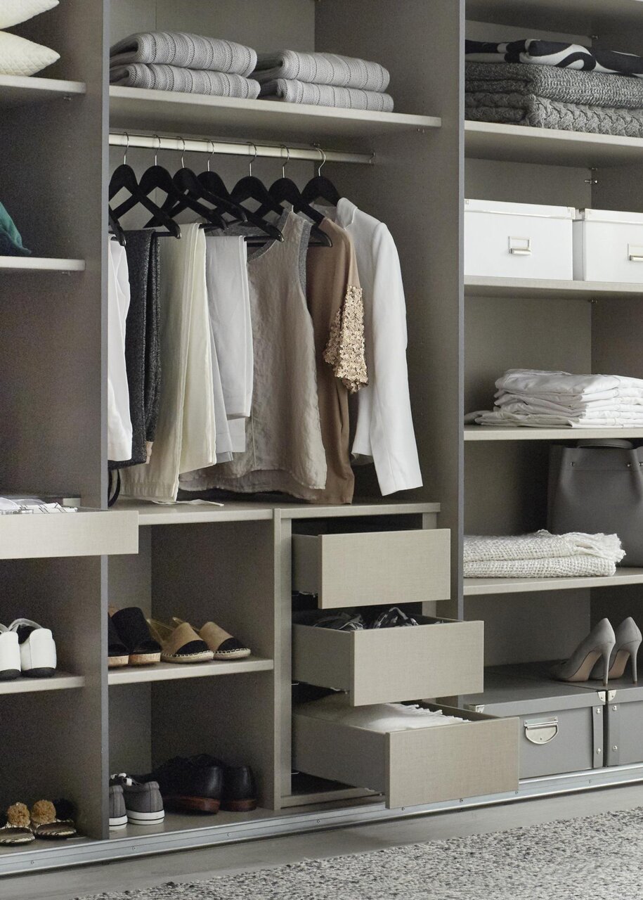 Open kledingkast met hangende kleding, planken met opgevouwen handdoeken en schoenen, en open lades. Aanzicht van voren.
