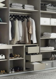 Open kledingkast met hangende kleding, planken met opgevouwen handdoeken en schoenen, en open lades. Aanzicht van voren.