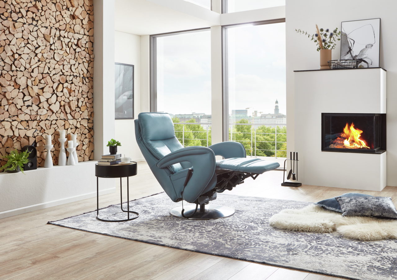 Moderner blauer Relax-Sessel in einem stilvollen Wohnzimmer mit Kamin und Panoramafenster, seitliche Perspektive.