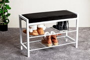 Weiße Schuhbank mit schwarzem Sitzpolster und zwei Drahtablagen, bestückt mit Schuhen, im Eingangsbereich auf grauem Teppich – Perspektive: seitliche Frontansicht leicht von oben.