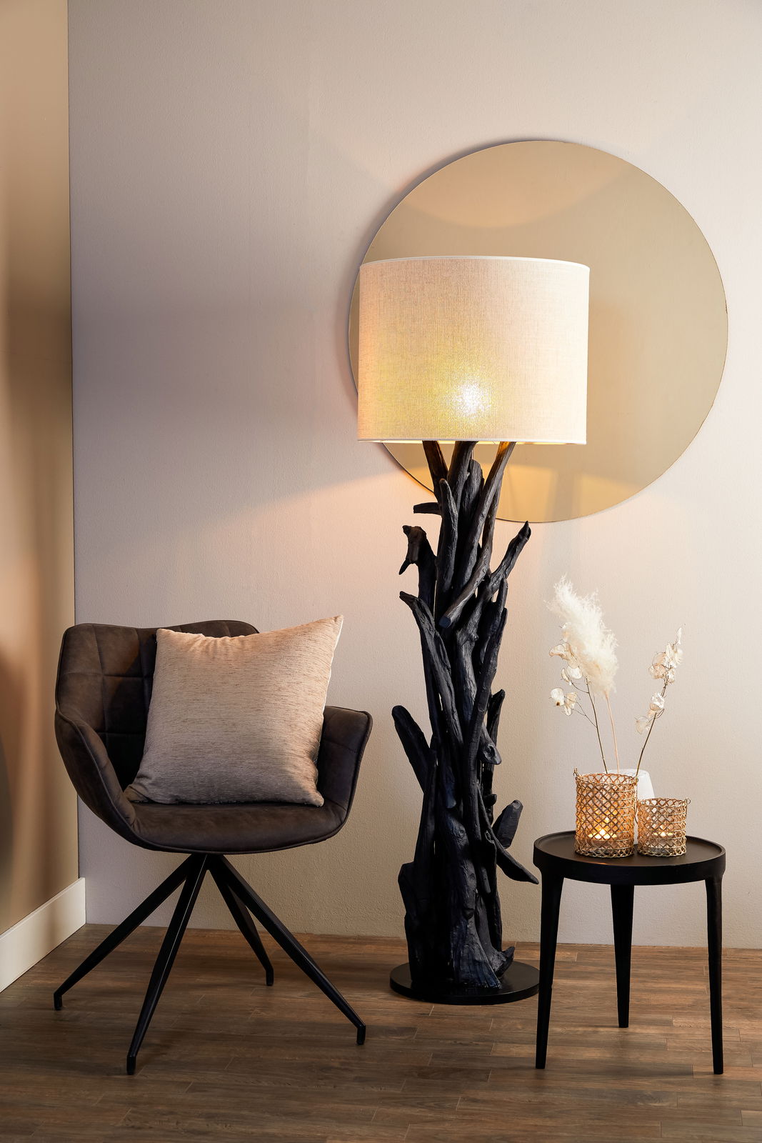 Stehlampe mit natürlichem Holzfuß und hellem Lampenschirm, seitliche Perspektive, neben einem Sessel und einem kleinen Tisch mit Dekoration.