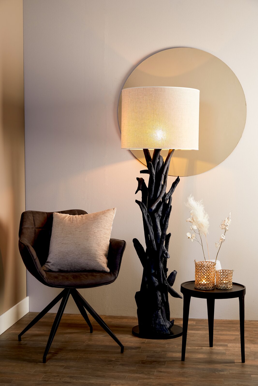 Stehlampe mit natürlichem Holzfuß und hellem Lampenschirm, seitliche Perspektive, neben einem Sessel und einem kleinen Tisch mit Dekoration.