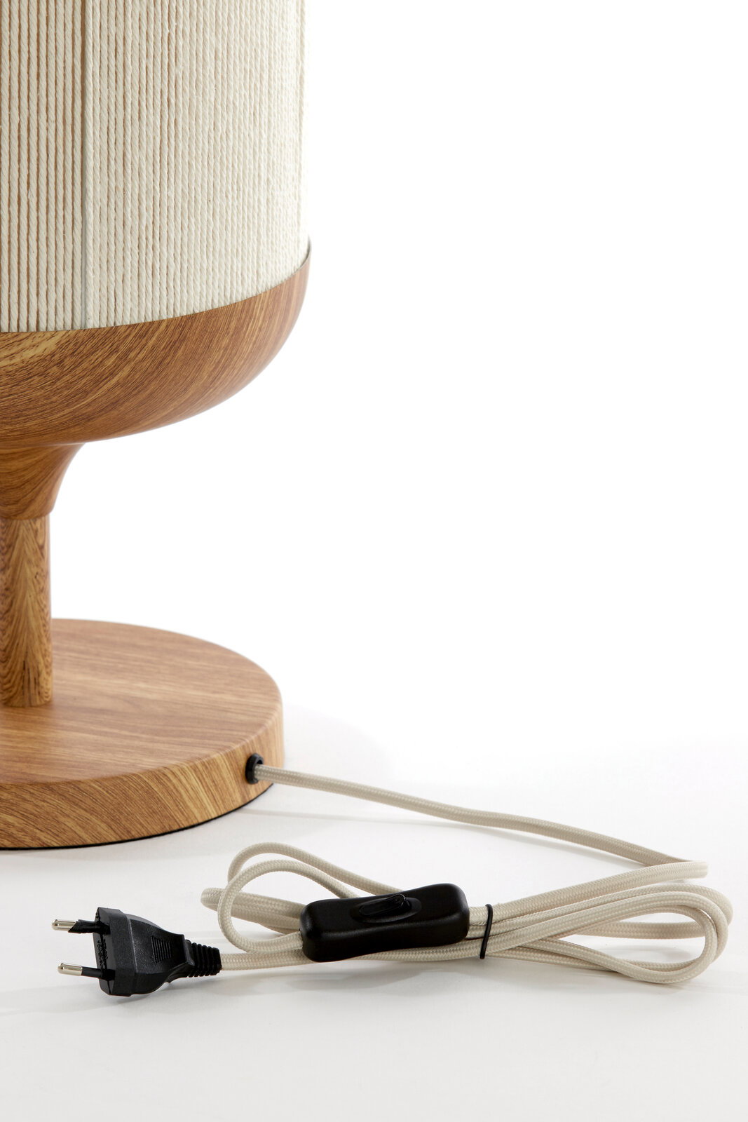 Detailaufnahme einer Tischlampe mit Holzfuß und beigefarbenem, strukturiertem Lampenschirm; sichtbares Textilkabel mit schwarzem Zwischenschalter und EU-Stecker, seitliche Perspektive