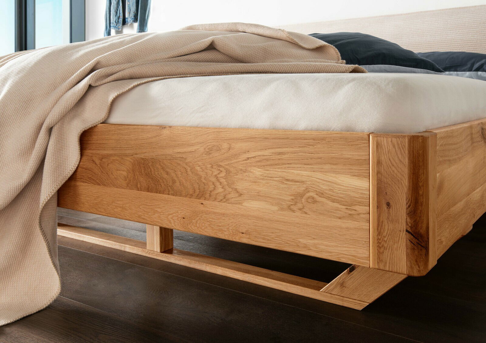 Massivholzbettgestell aus hellem Holz, seitliche Perspektive, mit Bettdecke und Kissen.