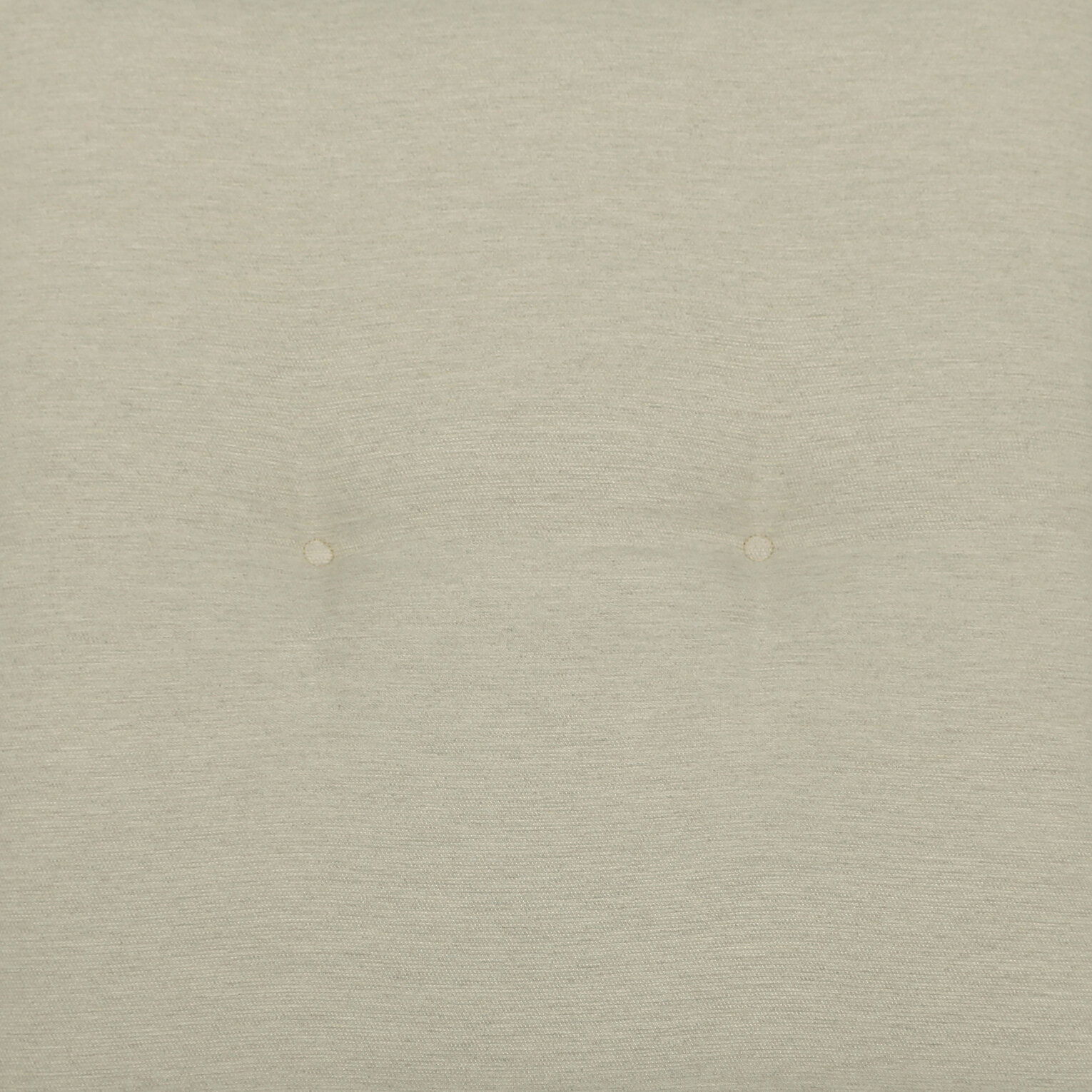 Nahaufnahme der hellbeigen, gepolsterten Stoffoberfläche mit zwei Knopfheftungen, frontal von oben fotografiert.