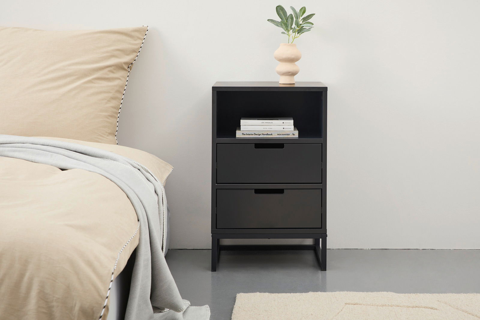 Novel Nachtkonsole hoch KUNO Schwarze Nachtkonsole mit zwei Schubladen und einem offenen Fach, darauf eine Vase mit Pflanze, seitliche Perspektive