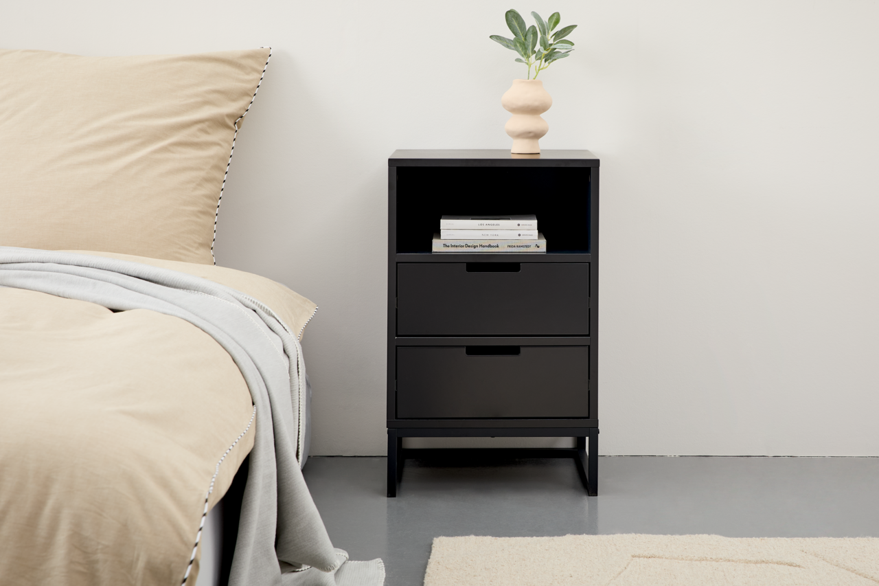 Novel Nachtkonsole hoch KUNO Schwarze Nachtkonsole mit zwei Schubladen und einem offenen Fach, darauf eine Vase mit Pflanze, seitliche Perspektive