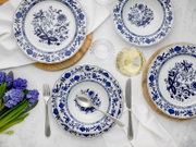 Blau-weißes Porzellan-Tafelservice mit floralen Mustern, Teller und Schale auf gedecktem Tisch mit Besteck, Glas und Blumen, Draufsicht von oben