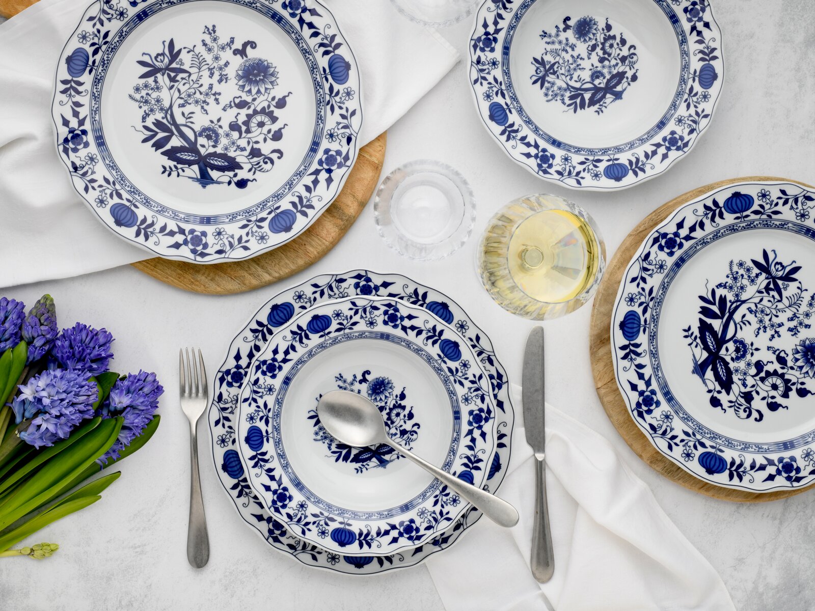 Blau-weißes Porzellan-Tafelservice mit floralen Mustern, Teller und Schale auf gedecktem Tisch mit Besteck, Glas und Blumen, Draufsicht von oben