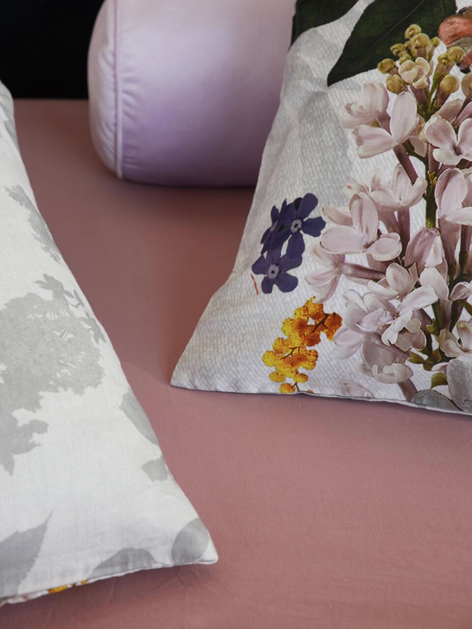 Nahaufnahme von Bettwäsche mit floralem Muster in Pastellfarben auf einem rosa Bettlaken, seitliche Perspektive