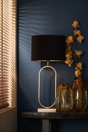 Eleganter Tisch mit einem ovalen Lampenschirm in Schwarz und goldener Basis, daneben dekorative Glasvasen und gelbe Trockenblumen, seitliche Perspektive.