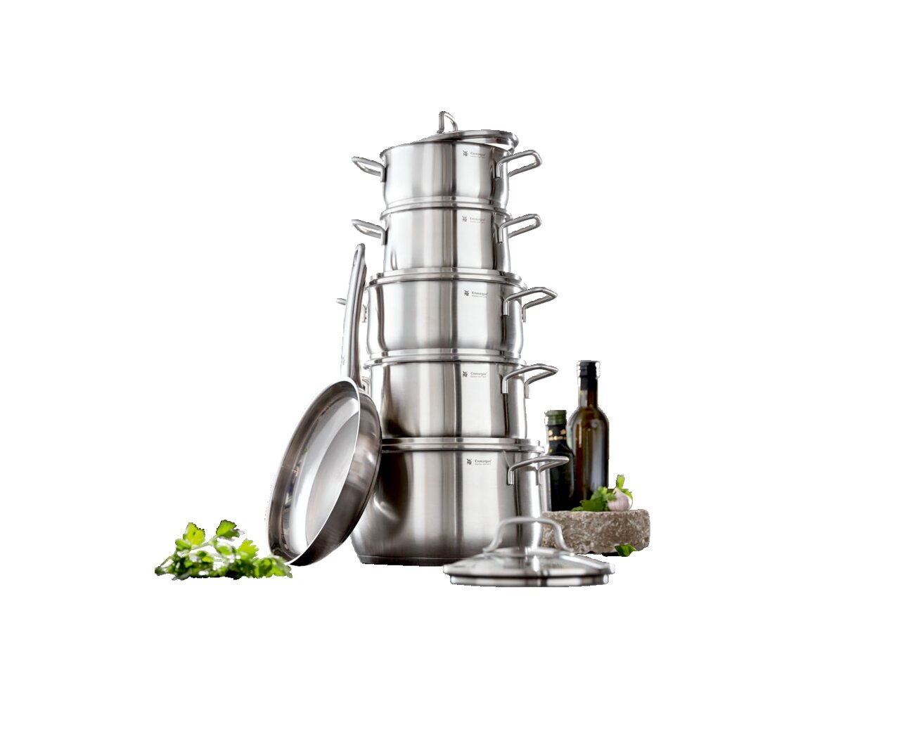 Stapel von Edelstahlkochtöpfen mit Deckeln, seitliche Perspektive, in einer modernen Küche mit frischen Zutaten im Vordergrund.