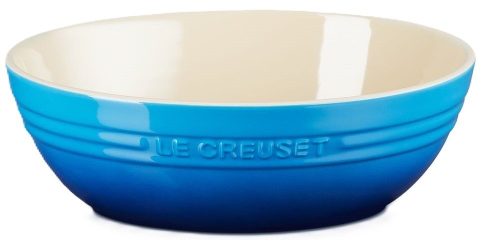 LE CREUSET Servierschale Blaue Le Creuset Keramikschüssel mit cremefarbener Innenseite und geprägtem Logo, freigestellt vor weißem Hintergrund, seitliche Ansicht leicht von oben