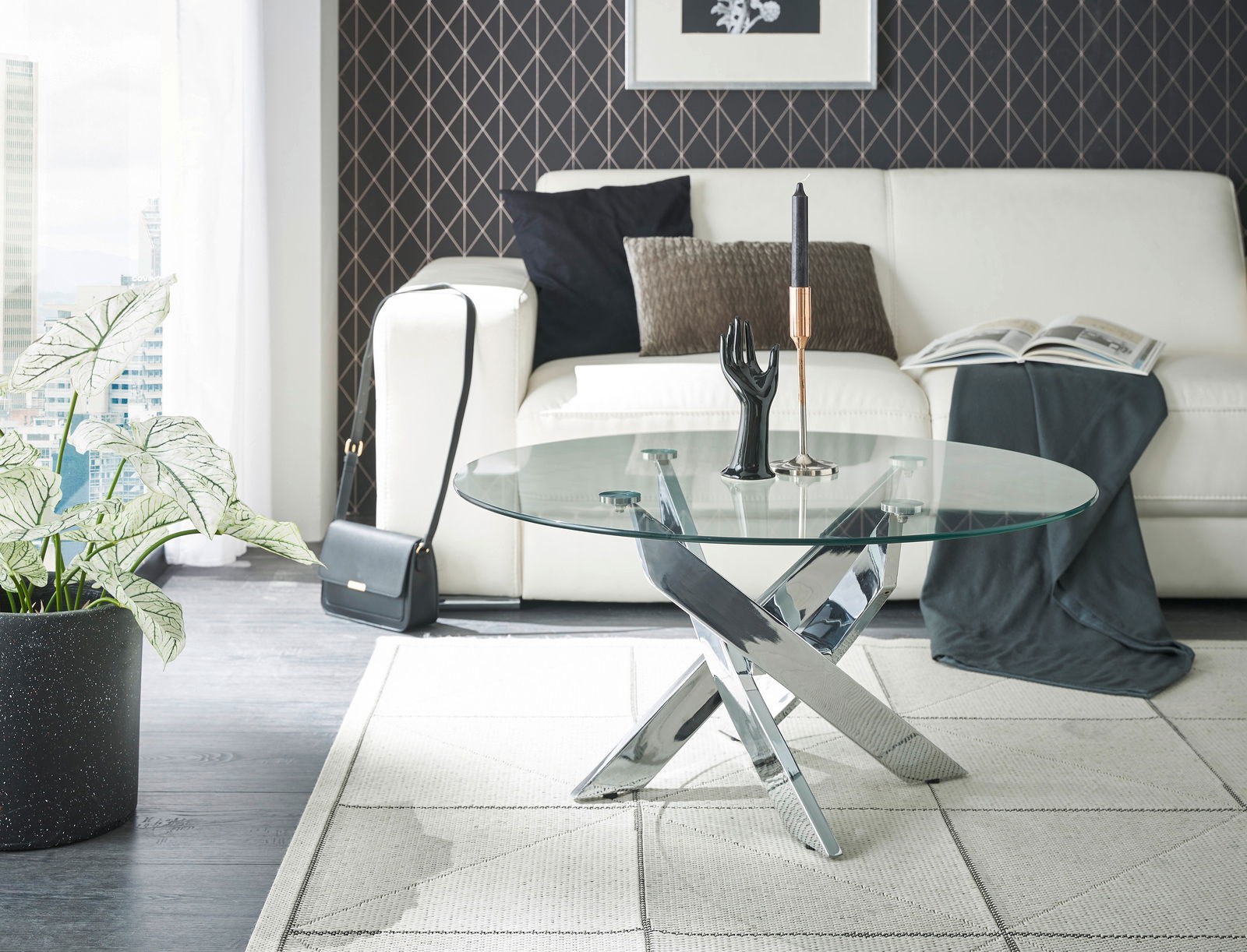 Moderner Couchtisch mit runder Glasplatte und verchromtem Kreuzfuß, im Wohnzimmer mit weißem Sofa und Dekorationen, seitliche Perspektive