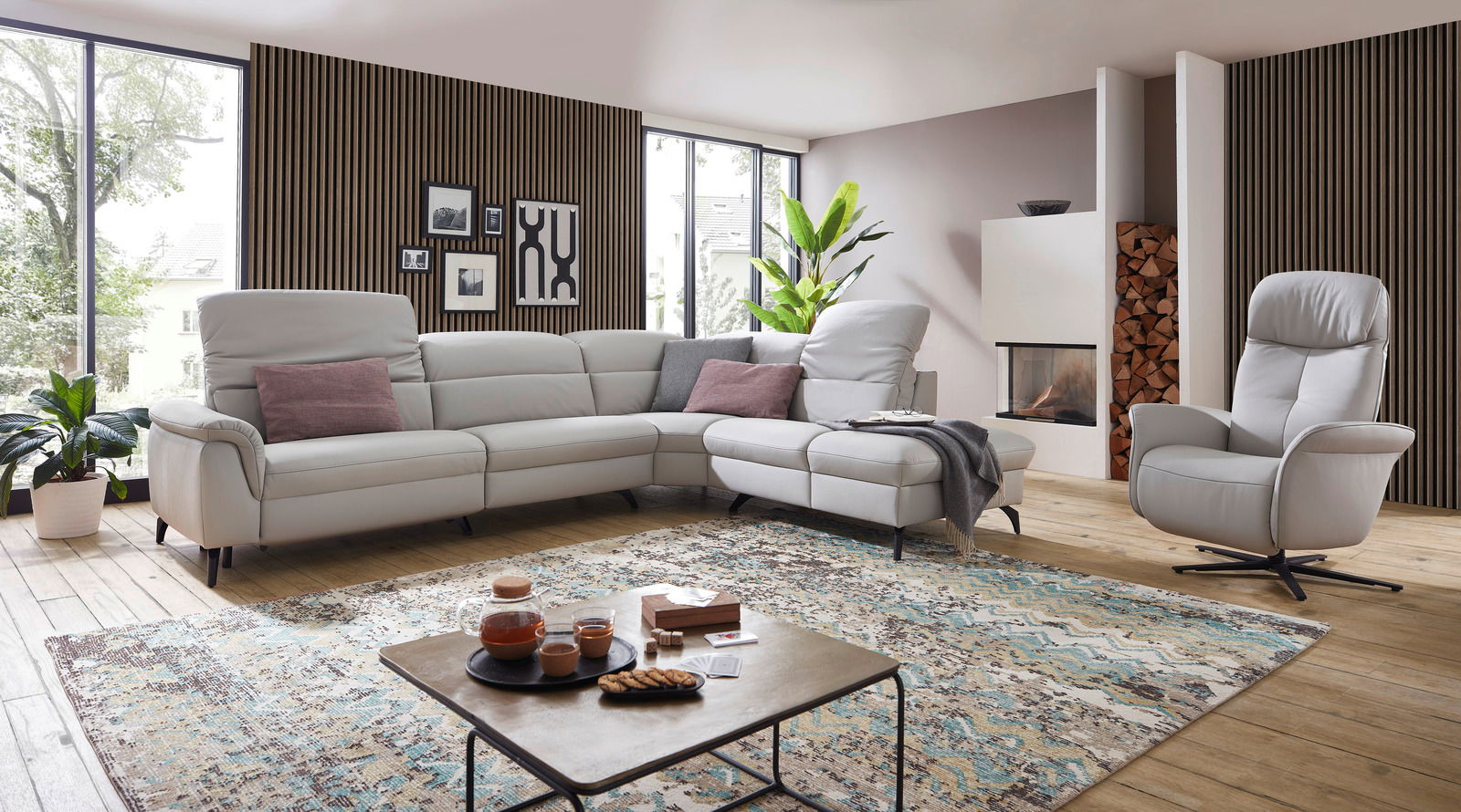 Eckgarnitur in einem modernen Wohnzimmer mit großen Fenstern, Holzboden und einem gemütlichen Sessel, seitliche Perspektive.