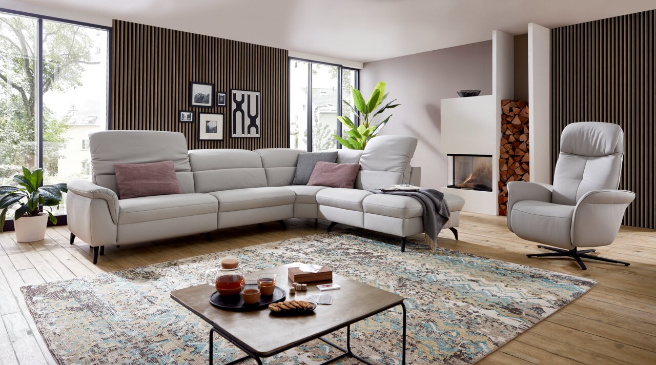 Eckgarnitur in einem modernen Wohnzimmer mit großen Fenstern, Holzboden und einem gemütlichen Sessel, seitliche Perspektive.